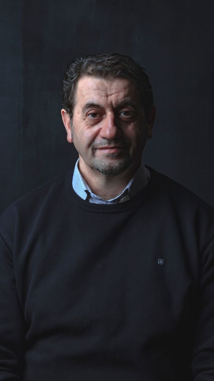 Studio portrait of a middle-aged man smiling in a black sweater against a dark background.